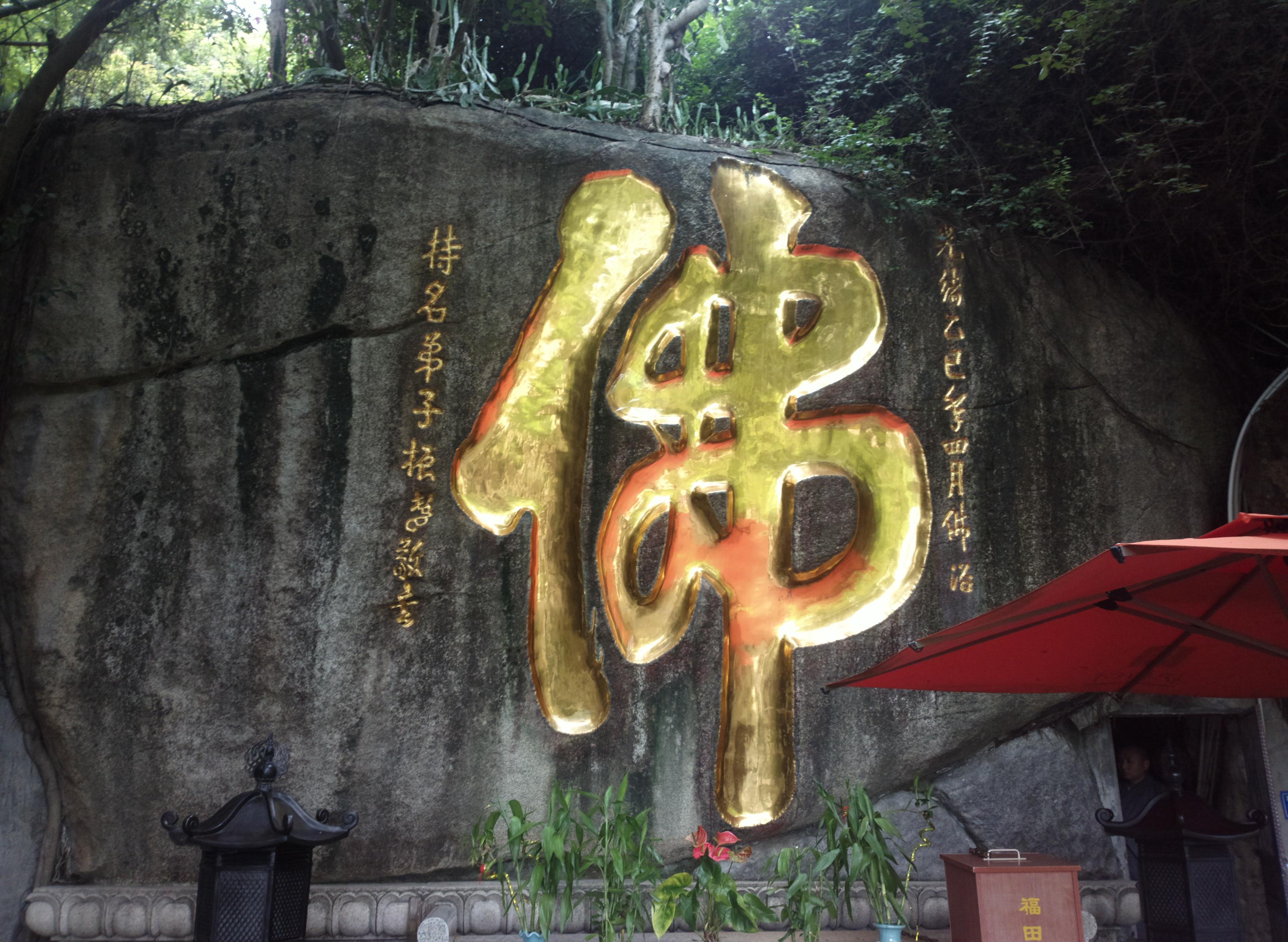 Traditional temple entrance with a large golden '福' (Fu) symbol on the rock, featuring lanterns and plants.